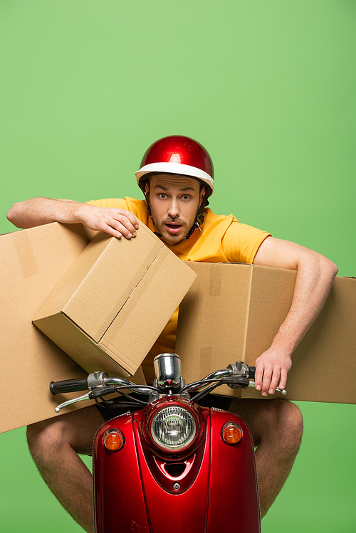 mad delivery man in yellow uniform on scooter with boxes isolated on green