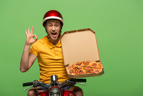 winking delivery man in yellow uniform on scooter with pizza showing ok sign isolated on green