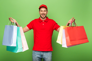 happy delivery man in red uniform holding shopping bags on green