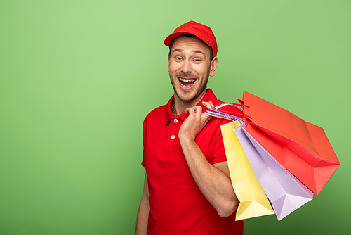 excited delivery man in red uniform holding shopping bags on green