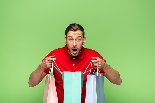 shocked young man holding shopping bags isolated on green