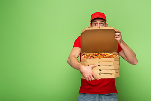 shocked delivery man in red uniform hiding behind pizza boxes on green