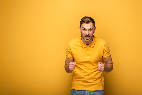 angry man in yellow outfit showing fists on yellow background