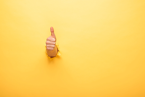 cropped view of man showing thumb up through yellow paper hole