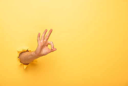cropped view of man showing ok sign through yellow paper hole