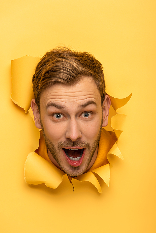 excited handsome man with head in yellow paper hole