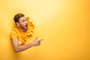 crazy handsome man in yellow outfit in yellow paper hole pointing with finger aside