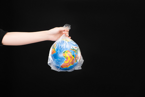 Cropped view of woman holding plastic bag with globe isolated on black, global warming concept