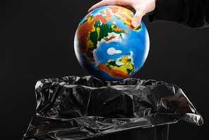 Cropped view of woman throwing away globe in trash bin isolated on black, global warming concept