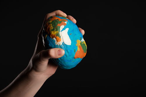 Cropped view of plasticine globe in female hand isolated on black, global warming concept
