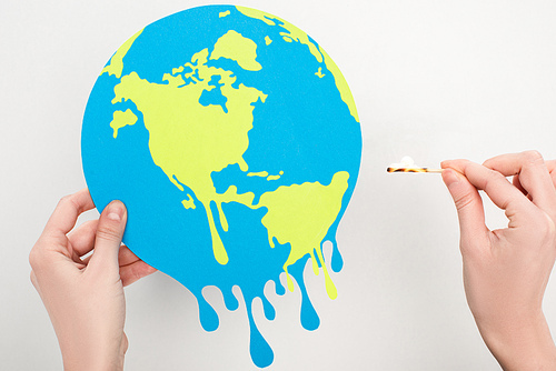 Cropped view of woman holding paper globe and match with fire on white, global warming concept