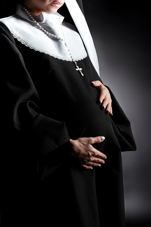 cropped view of pregnant nun touching tummy on grey