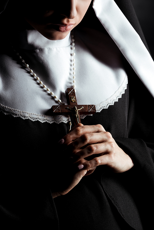 cropped view of young nun holding cross isolated on black