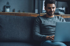 Smiling man watching pornography on laptop while sitting on couch in living room