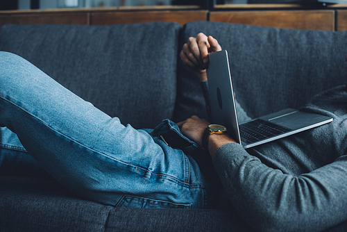 Cropped view of man masturbating while watching pornography on laptop on couch in living room