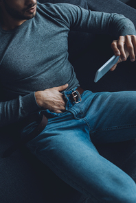 Cropped view of man watching pornography on smartphone and masturbating on couch