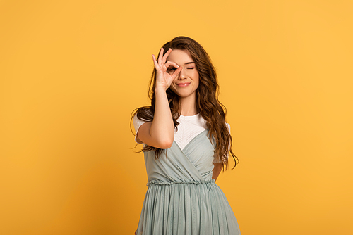 cheerful young spring woman showing ok sign on yellow