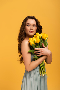 beautiful smiling woman in spring dress holding bouquet of tulip flowers isolated on yellow