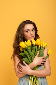 beautiful girl in spring dress holding bouquet of tulip flowers isolated on yellow