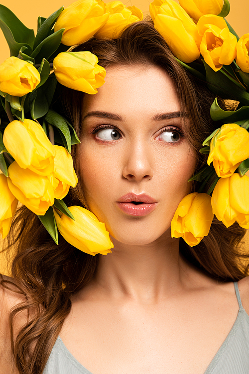 beautiful surprised girl in fresh tulip flowers isolated on yellow