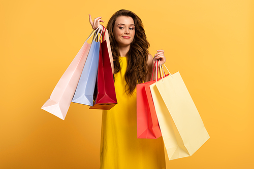 beautiful smiling girl in spring dress holding shopping bags on yellow