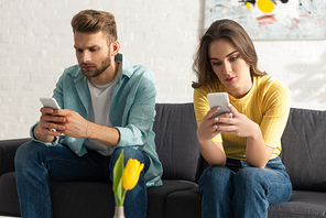 Selective focus of young couple using smartphones while sitting on couch at home