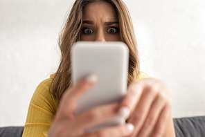 Selective focus of shocked girl using smartphone at home