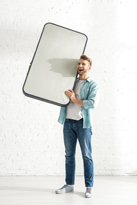 Cheerful man holding big model of smartphone at home