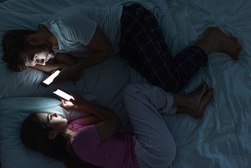 Top view of couple lying on bed with smartphones at night