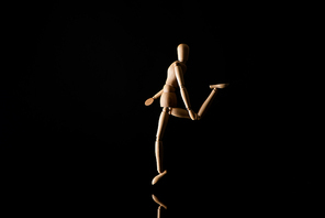 Wooden doll imitating raising leg on black background