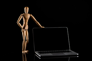 Wooden doll in standing position with hand on hip near laptop on black