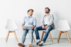 Man with laptop looking at laughing candidate on chair while waiting for job interview in office