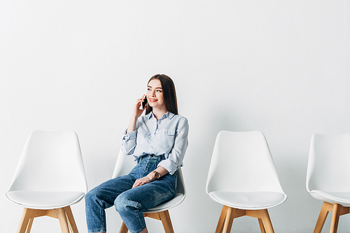 Smiling woman talking on smartphone while waiting job interview in office