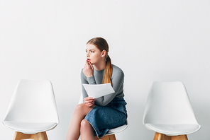 Pensive candidate holding resume while waiting job interview in office