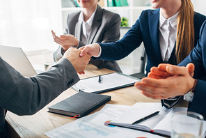 Cropped view of employee shaking hands with recruiter near colleagues during job interview
