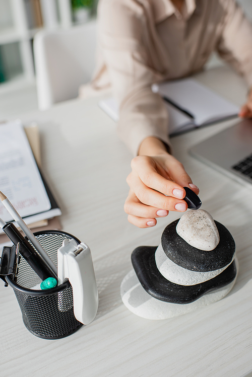 cropped view of businesswoman working with laptop at workplace with zen stones