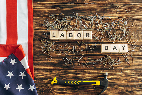 top view of metallic nails and hammer near american flag and cubes with labor day lettering on wooden surface