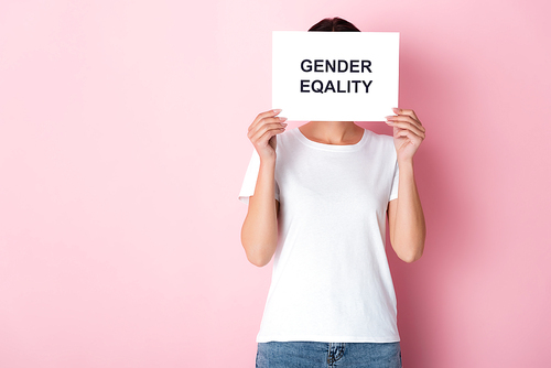 woman in white t-shirt covering face with gender  lettering on placard and standing on pink