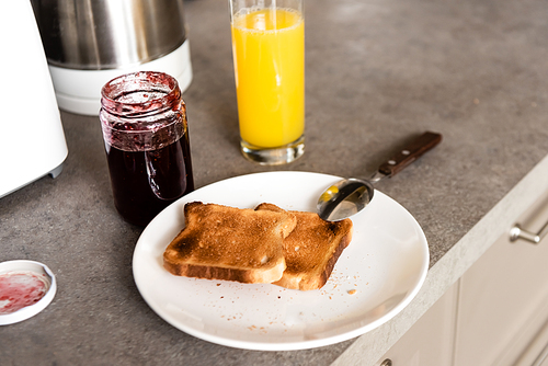 plate with tasty toasts and spoon near jar with jam and glass with orange juice