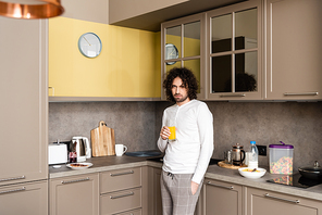 sad man in pajamas  while holding glass of orange juice in kitchen