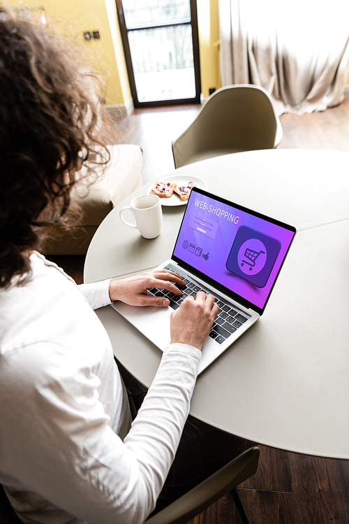 high angle view of freelancer using laptop with web shopping website near coffee cup and plate with toasts