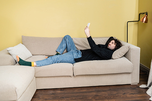 Side view of handsome man using smartphone while lying on couch at home