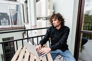 Handsome freelancer using laptop on balcony at home