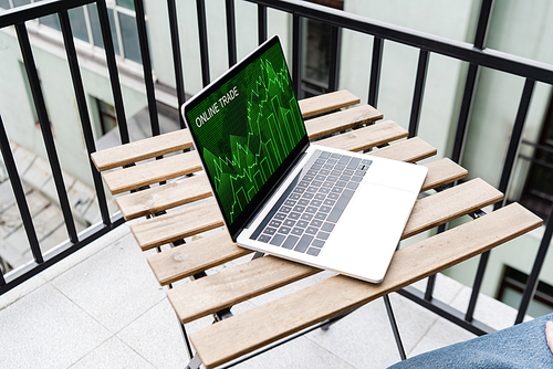 Cropped view of man sitting near laptop with online trade website on balcony