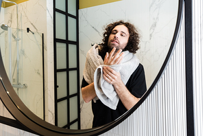 Handsome man looking at mirror while holding towel in bathroom