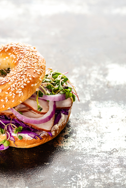 fresh delicious bagel with meat, red onion, cream cheese and sprouts on textured grey surface