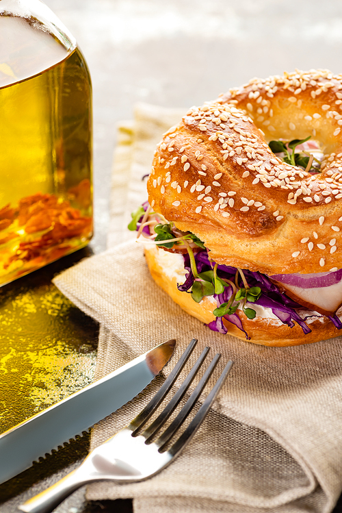 fresh delicious bagel with meat, red onion, cream cheese and sprouts on napkin with cutlery on textured surface