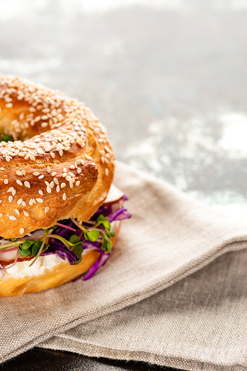 fresh delicious bagel with meat, red onion, cream cheese and sprouts on napkin on textured surface