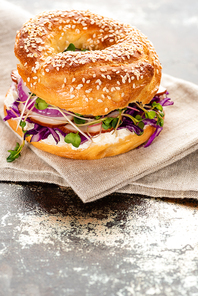 fresh delicious bagel with meat, red onion, cream cheese and sprouts on napkin on textured surface