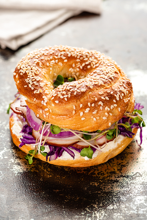 fresh delicious bagel with meat, red onion, cream cheese and sprouts on textured surface